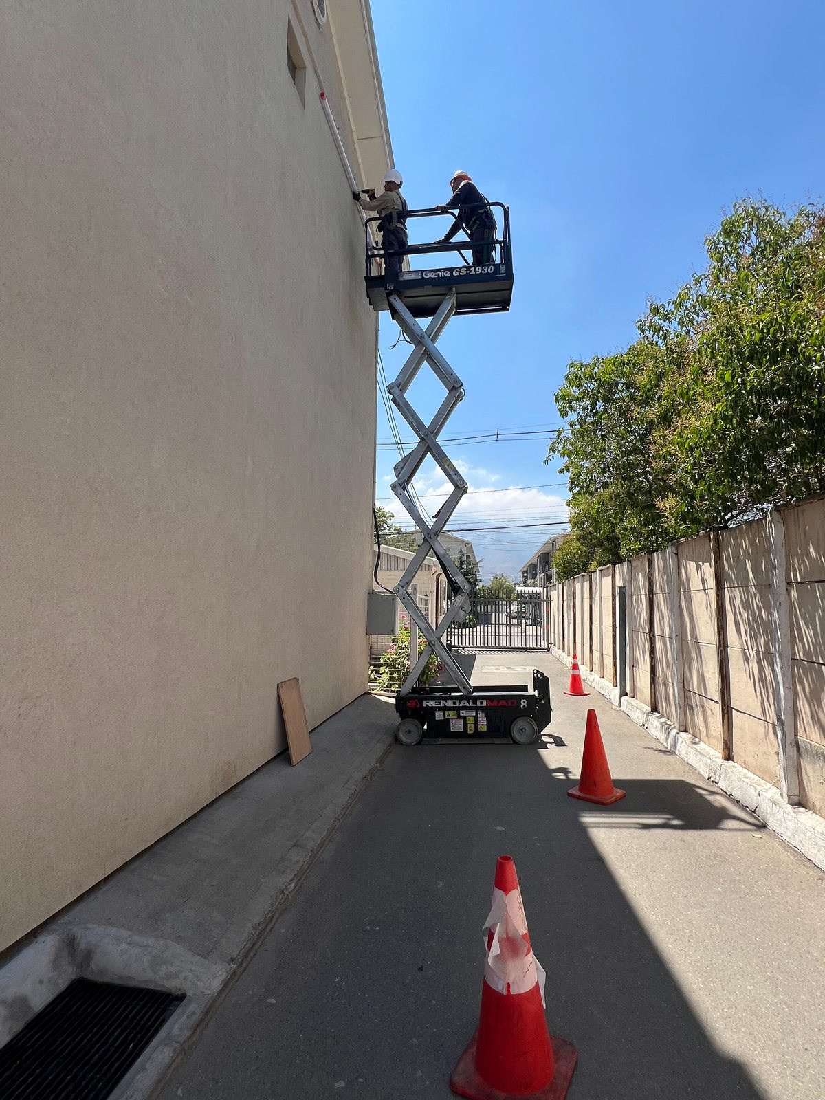 Dos técnicos de MCF trabajando desde un alzahombre Genie GS-1930 en la fachada de un edificio, con la zona delimitada por conos.
