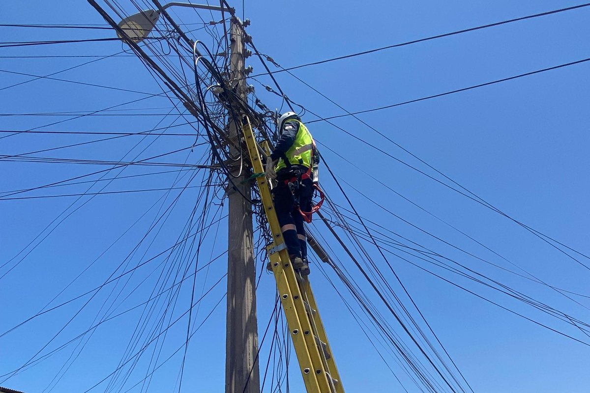 Técnico de MCF sobre una escala, trabajando el cableado de un poste de distribución en una calle de Arica.